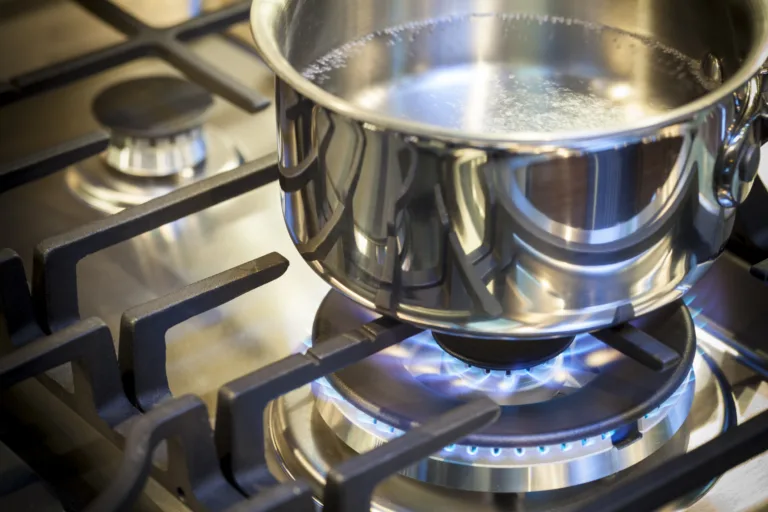 Gas burner on stove with flame on stainless steel surface showing heat ready for cooking food. Stainless steal pot on burner cooking food.