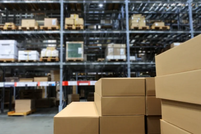Blurred background of many items inside cardboard boxes on warehouse storage shelves.