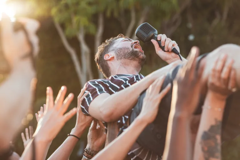 Crowd, surfing and man singing at party, outdoor music festival or social gathering. Microphone, energy and male singer diving in audience group at performance event, celebration or crazy fun weekend