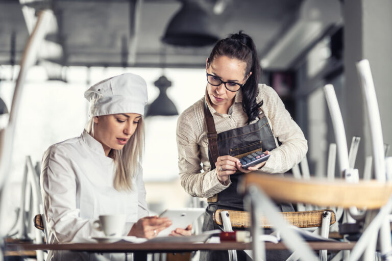 Female chef and waitress sit over bills calculating after hours in a restaurant.