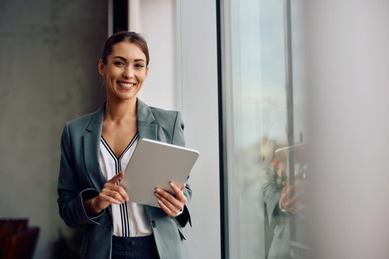 Happy female entrepreneur using touchpad while working in the office and looking at camera. Copy space.